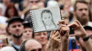 Bei einem Protest hält jemand eine Zeichnung von Greta Thunberg in die Luft.