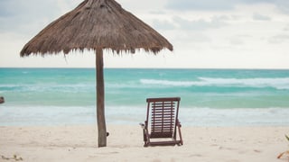 Sonnenschirm und Liegestuhl vor Meereskulisse.