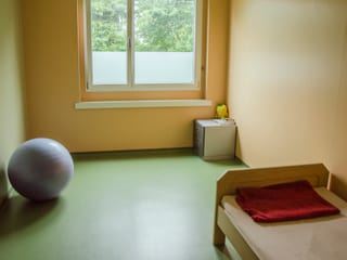 Schlichte Zimmereinrichtung mit Gymnastikball, Bett, Kommode und Plüschtier. 