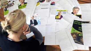 Eine Frau sitzt vor einem Haufen Wahlunterlagen.