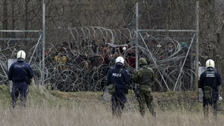 Griechische Polizisten stehen vor einem Grenzzaun, dahinter Migranten Griechische Polizisten stehen vor einem Grenzzaun, dahinter Migranten