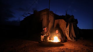 Zwei Menschen sitzen vor einem Zelt an einem Feuer.