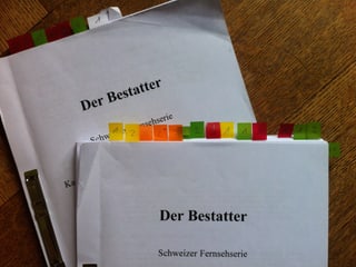 Zwei Drehbücher mit dem Titel «Der Bestatter». In den Büchern sind einige Seiten mit farbigen Post-Its markiert.