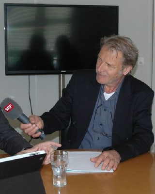 Reinhard Eyer sitzt am Tisch mit einem SRF-Mikrofon.