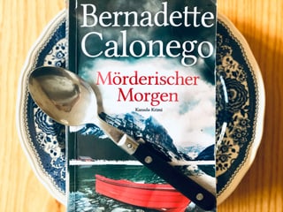 Der Krimi «Mörderischer Morgen» liegt auf einem blau gemusterten Suppenteller. Ein Esslöffel ist über das Buch gelegt. Der Krimi «Mörderischer Morgen» liegt auf einem blau gemusterten Suppenteller. Ein Esslöffel ist über das Buch gelegt.