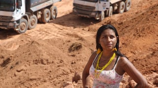 Eine dunkelhäutige Frau im Trägershirt steht mit angewinkelten Armen in einer Goldmine.