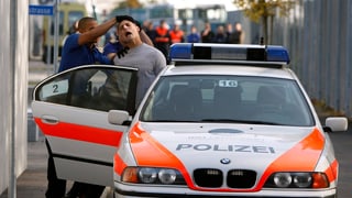 Ein Polizist stösst einen Zivilisten in ein Polizeiauto