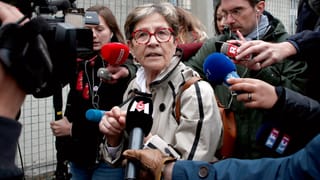 Viviane Lambert umringt von Reportern mit Mikrofonen.