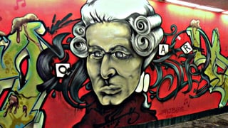 Ein buntes Graffito von Mozart auf rotem Hintergrund in einer Strassenunterführung.