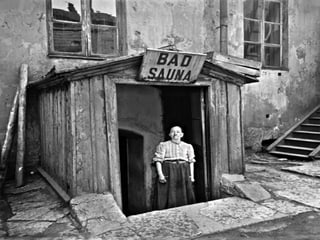  Eine Frau steht in der Türe eines Hauses, über der ein Schild mit der Aufschrift «Bad/Sauna» angebracht ist.