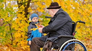 älterer Mann im Rollstuhl mit Kind im Wald