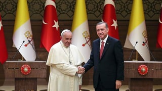 Papst Franziskus (links) und Recet Tayyip Erdogan (rechts) stehen nebeneinander vor den Fahnen vom Vatikan-Staat und der Türkei.
