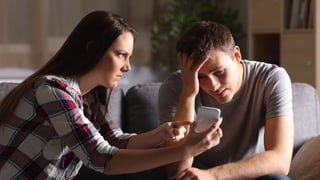 Eine Frau hält ihrem Partner das Smartphone vors Gesicht und macht einen vorwurfsvollen Gesichtsausdruck.