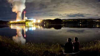 Zwei Personen sitzen am Abend am Rhein vor dem Kernkraftwerk Leibstadt.