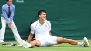 Novak Djokovic mit verzerrtem Gesicht am Boden sitzend.
