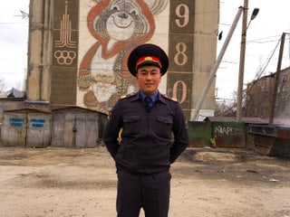 Beamter vor einer Hauswand, die verziert ist mit dem Logo der olympischen Spiele aus Zeiten der Sowjetunion