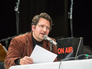 Ein Mann auf der Bühne vor einem Mikrofon mit Blatt Papier in der Hand.