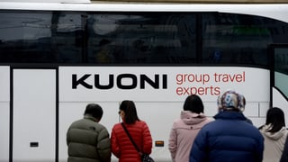 Reisebus mit Auschrift Kuoni, davor von hinten fotografiert wartende Reisende