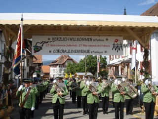 Grün uniformierte Blasmusikanten marschieren musizierend durchs Dorf.