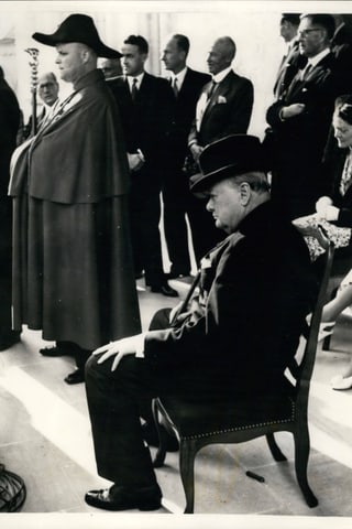 Churchill sitzt auf einem Stuhl, im Hintergrund steht ein Bundesweibel.