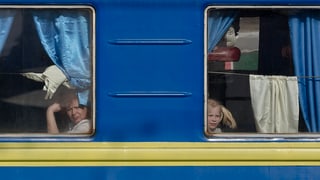 Ein Zug mit den Landesfarben der Ukraine. Zwei Passagiere schauen aus dem Fenster.