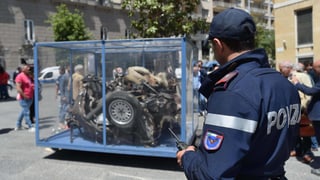 Autowrack in einem Glaskäfig, daneben steht ein Polizist. Autowrack in einem Glaskäfig, daneben steht ein Polizist.