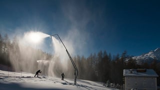 Skifahrer passieren in der Nacht eine Beschneiungsanlage in der Region St. Moritz.