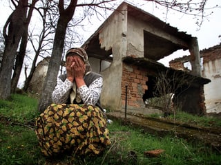 Eine Frau trauert vor ihrem zerstörten Haus.