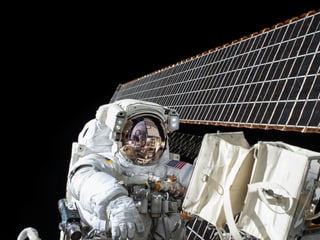 Ein Astronaut auf einer Aussenmission vor den Sonnensegeln der ISS.