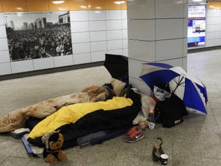 Zwei Personen in Schlafsäcken liegen in einer Unterführung.