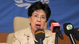 Asiatische Frau mit Brille spricht in drei Mikrophone.
