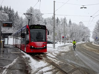 Schnee in Bern, eine Strassenbahn fährt zur Haltestelle, auf der Strasse liegt Schneematsch.