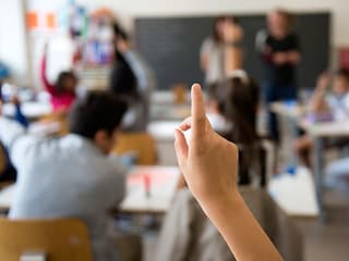 Eine Kinderhand streckt auf - im Hintergrund das Klassenzimmer