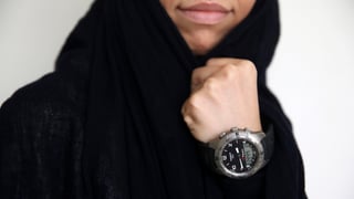 Eine Frau mit schwarzem Schleier zeigt ihre Tissot-Uhr, die sie am linken Handgelenk trägt.