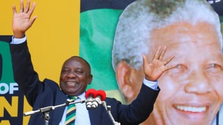 Ramaphosa gestikuliert vor Mikrofonen, hinter ihm eine Grossprojektion von Nelson Mandela.