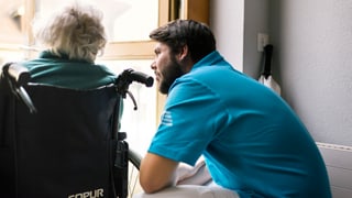 Zivildienstleistender spricht mit betagter Frau in Rollstuhl