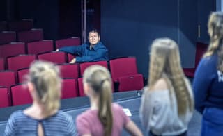 Vier Mädchen stehen auf der Theaterbühne, im Publikum sitzt der Schauspieler und Theatermacher Hanspeter Müller-Drossaart