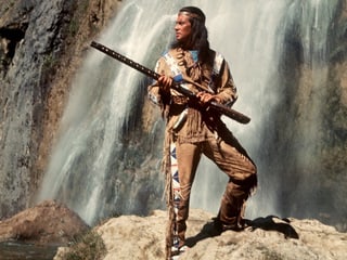 Pierre Brice als Winnetou vor einem Wasserfall. 