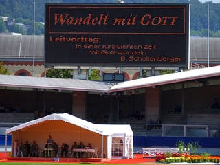 Ein Zelt steht in einem Fussballstadion, über dem eine Grossleinwand mit der Aufschrift «Wandelt mit Gott» steht.