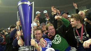 Eine Mannschaft von Hockey-Spielern jubelt, in der Bildmitte ein blauer Pokal und ein schreiender Mathias Seger.