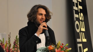 Ein Mann, ins Mikrofon sprechend, Blumen in der Hand. Ein Mann, ins Mikrofon sprechend, Blumen in der Hand.