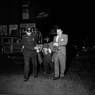 schwarz weiss Fotografie. zwei polizisten transportieren einen Betrunkenen Mann ab.