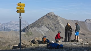 Wanderer stehen vor eine Wanderweg-Wegweiser in der Bergwelt.