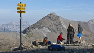 Wanderer stehen vor eine Wanderweg-Wegweiser in der Bergwelt. Wanderer stehen vor eine Wanderweg-Wegweiser in der Bergwelt.