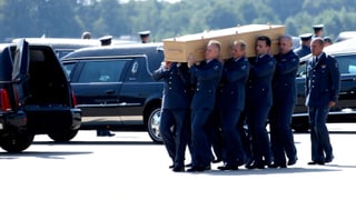 Männer tragen einen Sarg zum Leichenwagen.