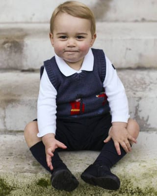 Prinz George in blauem Gilet auf einer Steintreppe sitzend.