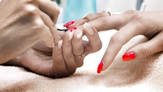Eine Frau lackiert einer anderen Frau die Fingernägel rot.
