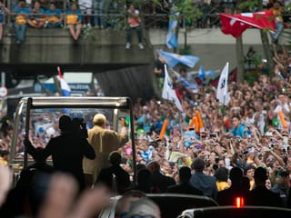 Das Papamobil von hinten gesehen, umringt von den Massen, die den Pontifex feiern.