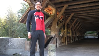 Ein Mann steht im Velotricot vor einer Holzbrücke.