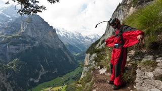 Ein Basejumper in rotem Anzug steht am Berg bereit zum Sprung.